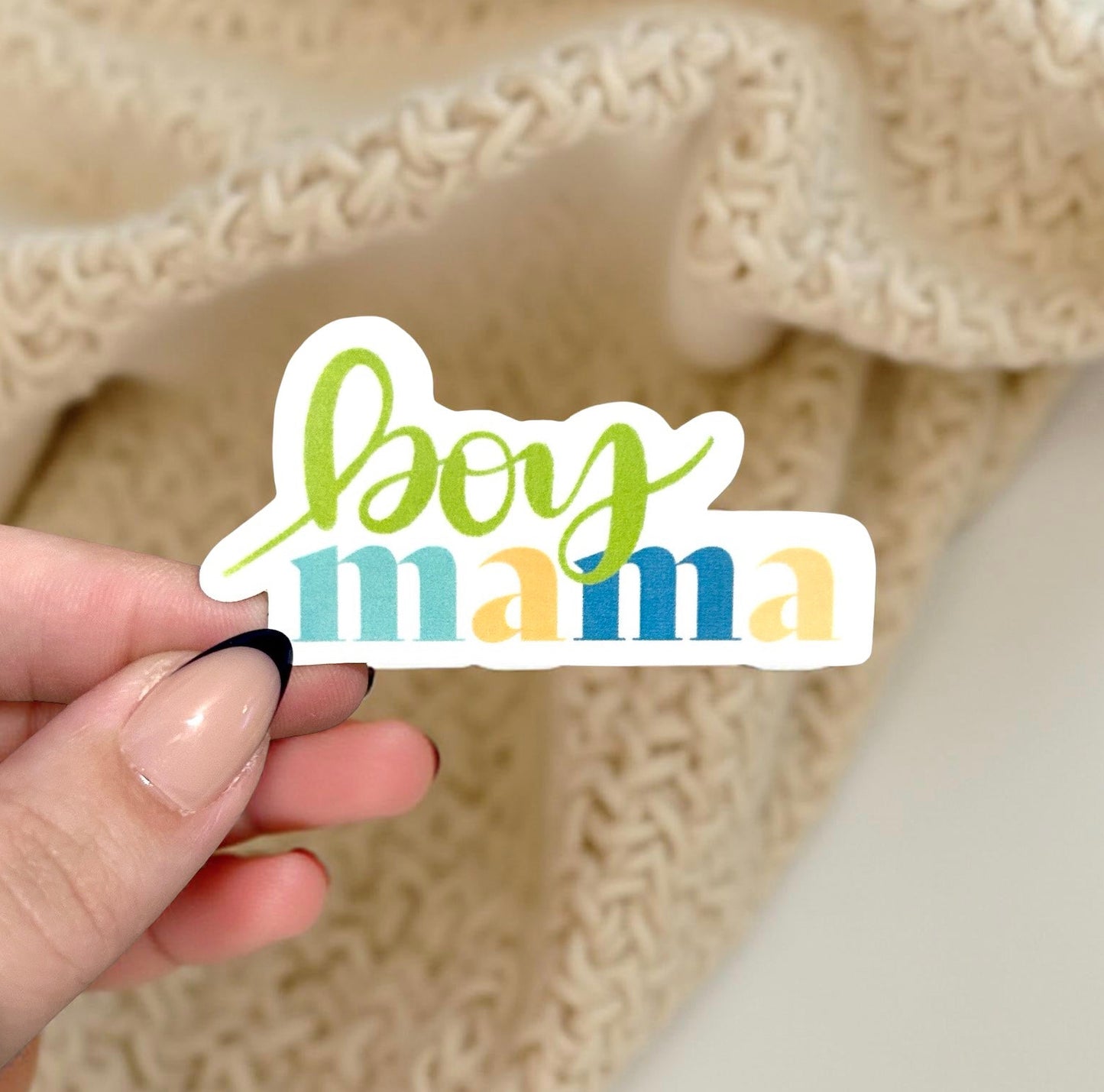 Hand holding a 'boy mama' sticker against a textured beige background