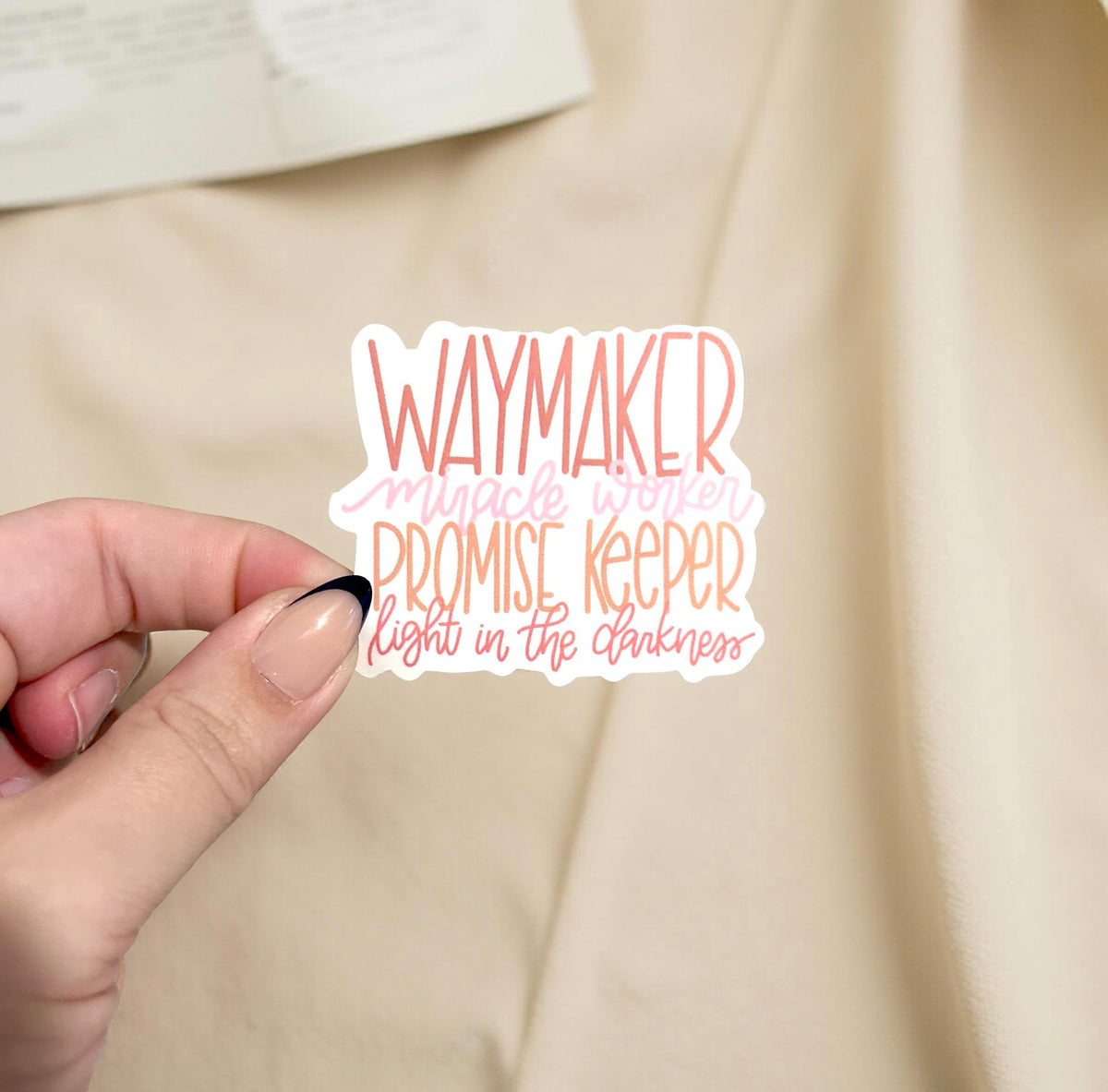 hand holding sticker with the lyrics to waymaker written in pink and orange