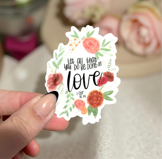 A hand holding a sticker with Bible verse let all things be done in love