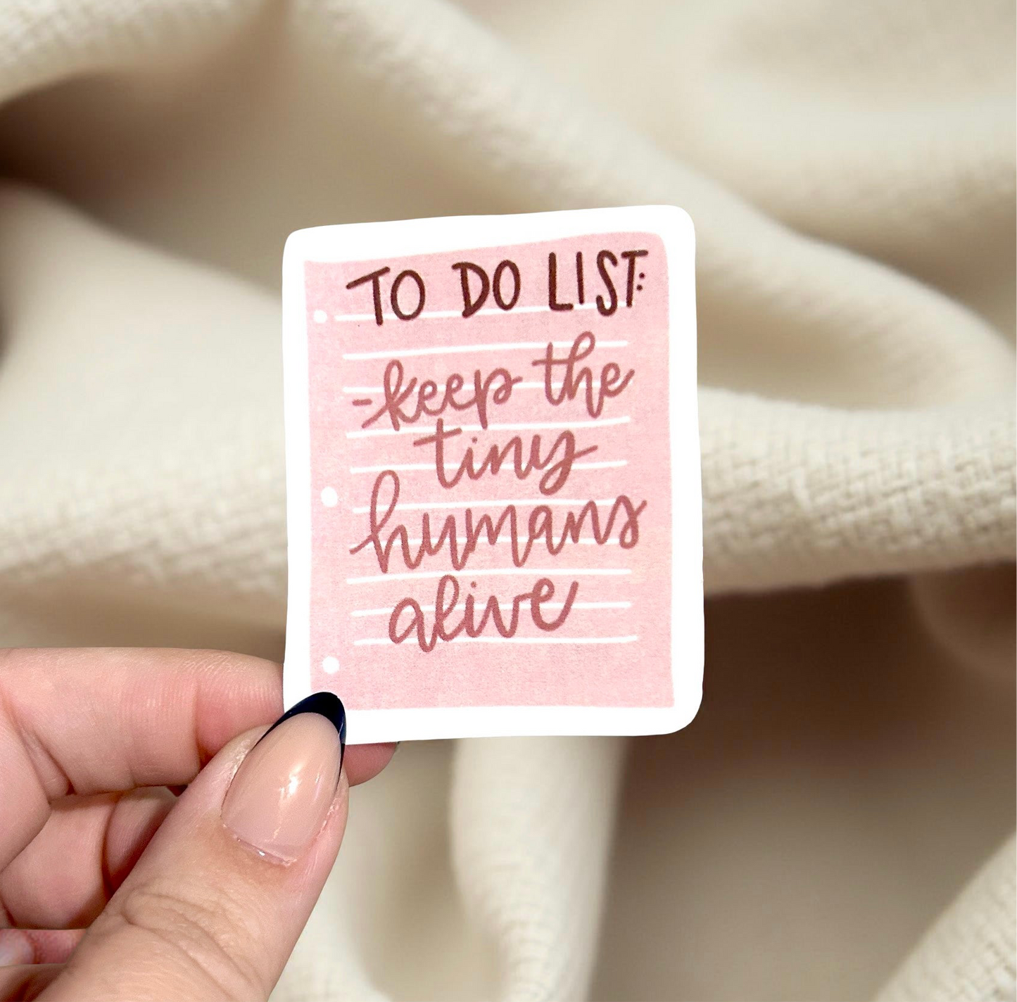 Hand holding a sticker that says to do list keep the tiny humans alive 