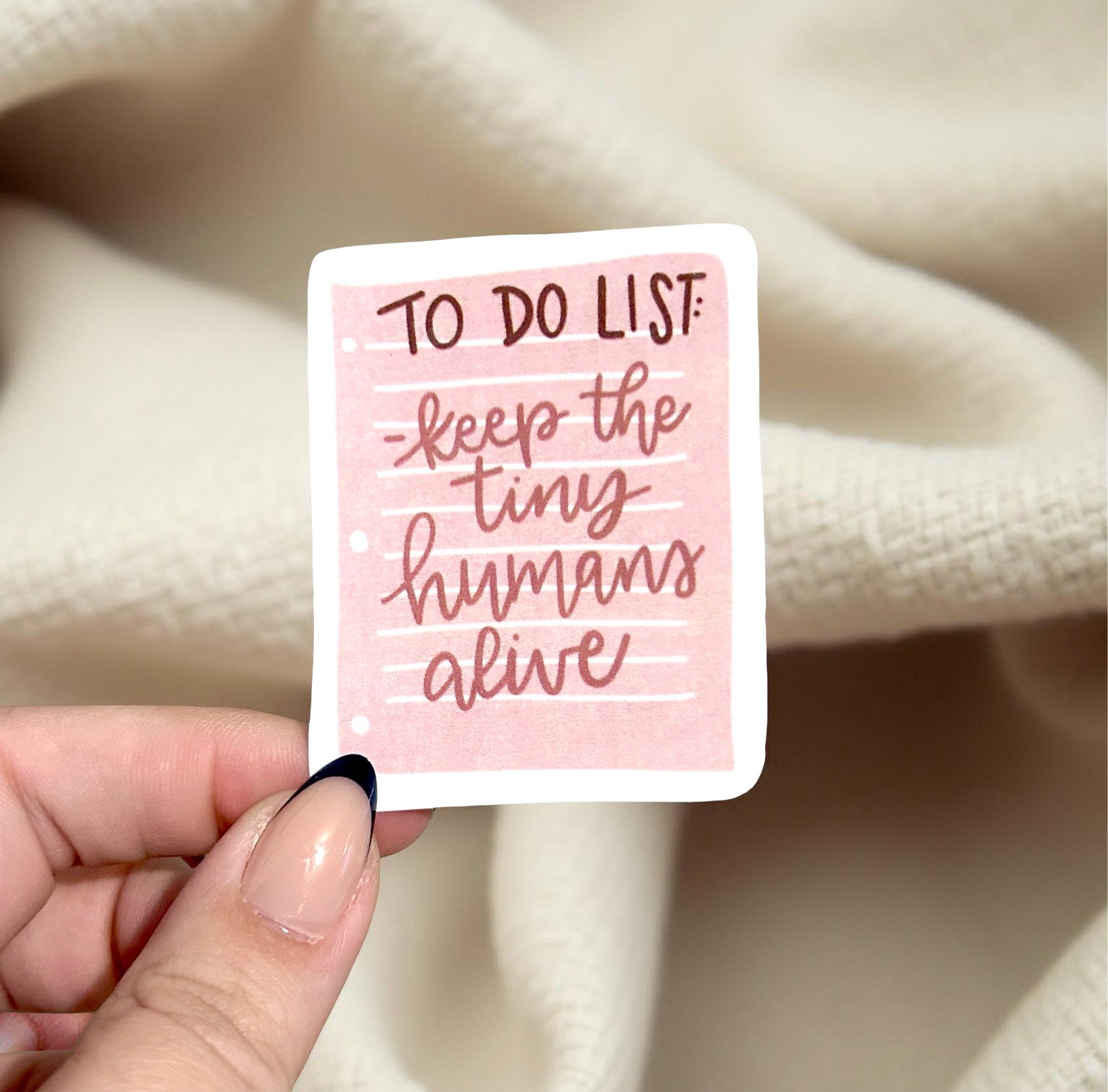 Hand holding a sticker that says to do list keep the tiny humans alive 