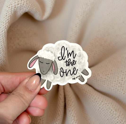 Sheep sticker with 'I'm the one' text held by a hand against a beige fabric background