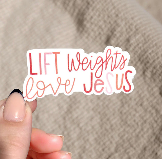 Hand holding a sticker with 'LIFT Weights love Jesus' text against a beige background
