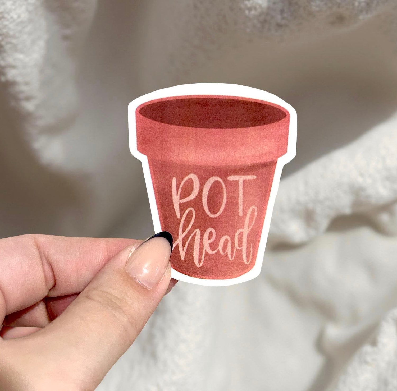Sticker of a red pot with 'POT head' text held by a hand against a textured white background