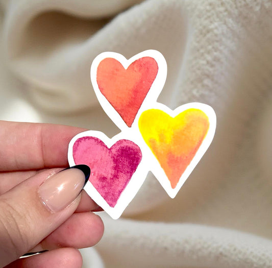 Hand holding three colorful heart-shaped stickers against a beige fabric background