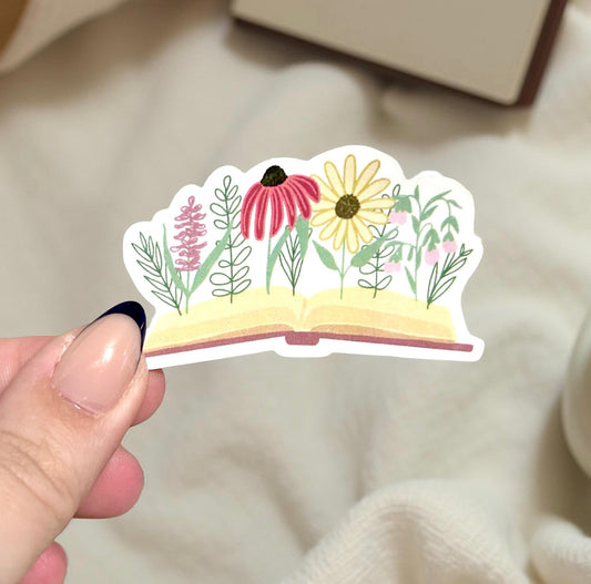 Hand holding a sticker of a book opening with flowers