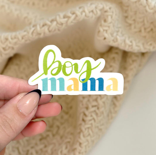 Hand holding a 'boy mama' sticker against a textured beige background